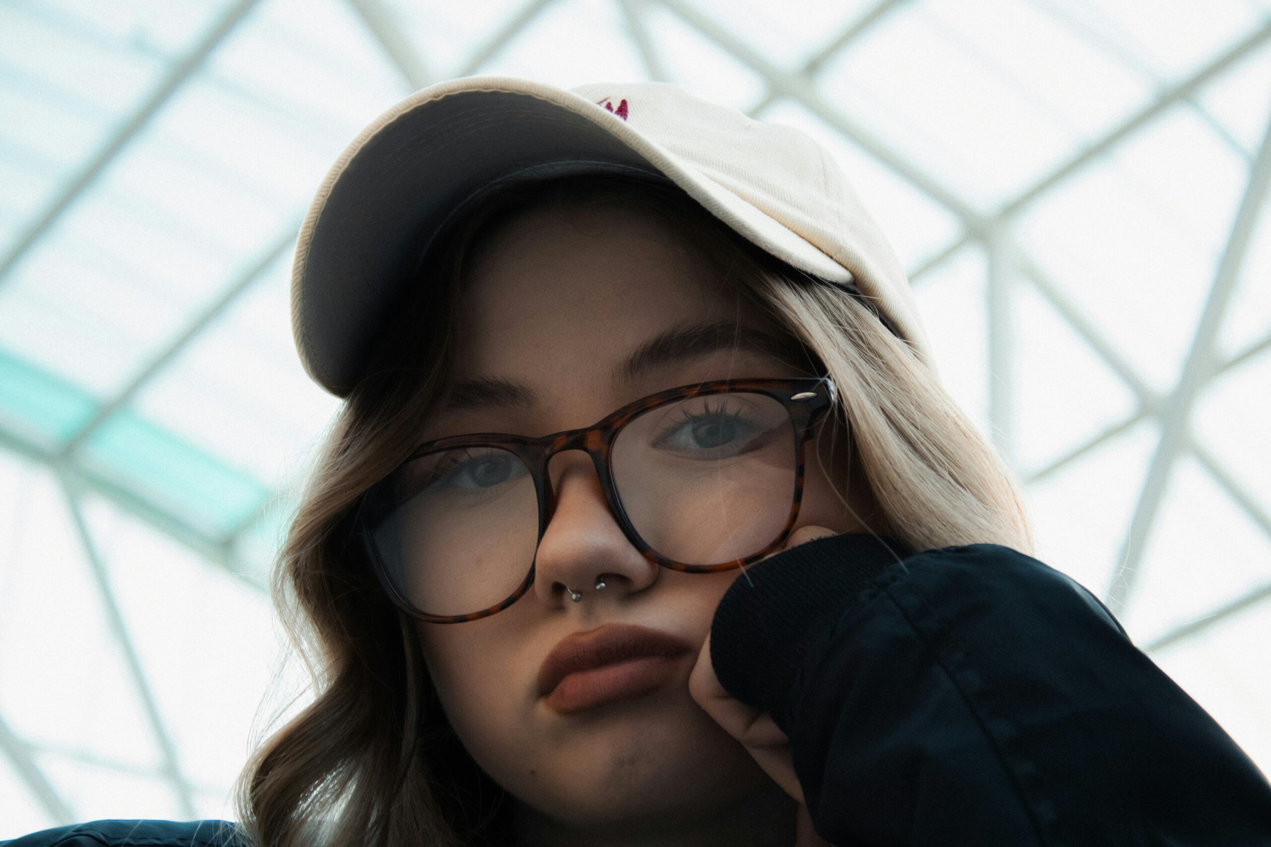 Young woman looking down at camera with glasses and a baseball hat on