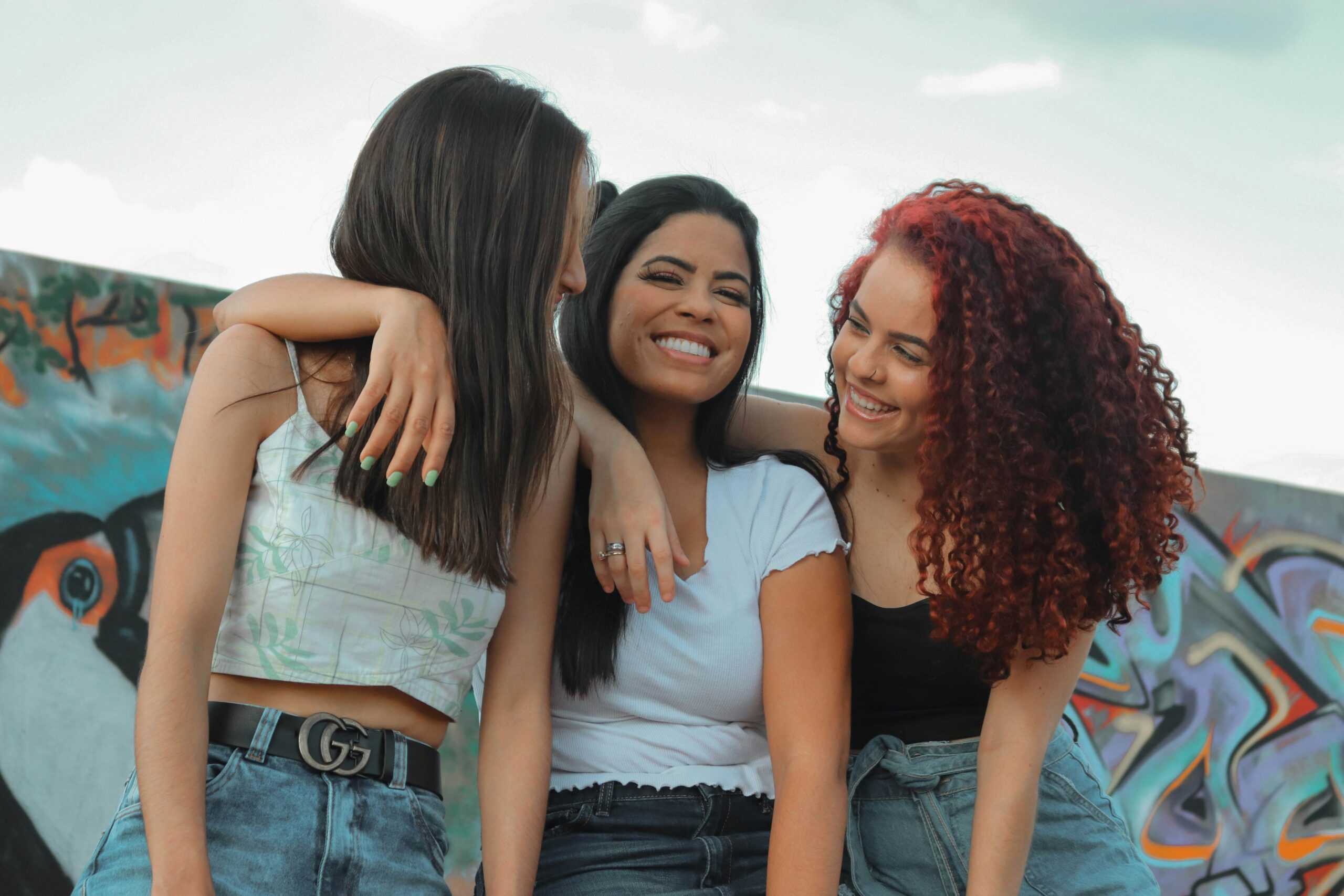 Three girls smiling at each other with their arms around each other.