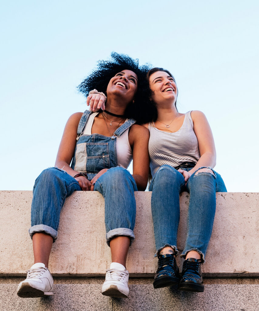 Two women sitting on a ledge, one with an arm around the other.