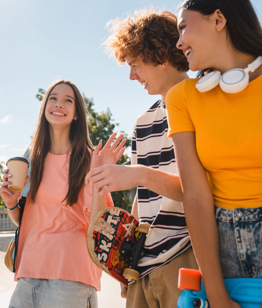 Three teens laughing with each other, walking at a skate park with skateboards in hand