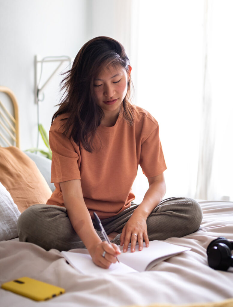 woman sitting on bed writing in a notebook