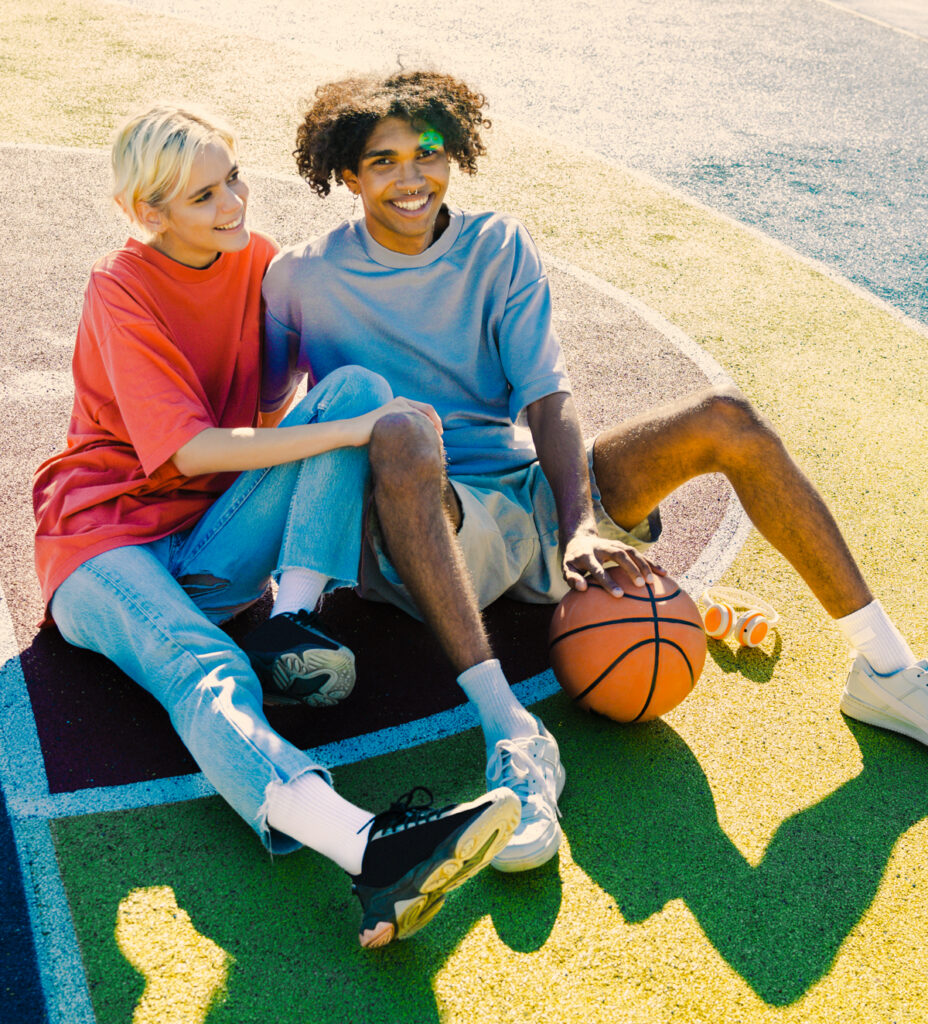 A young man and woman sitting on a basketball court next to each other, smiling