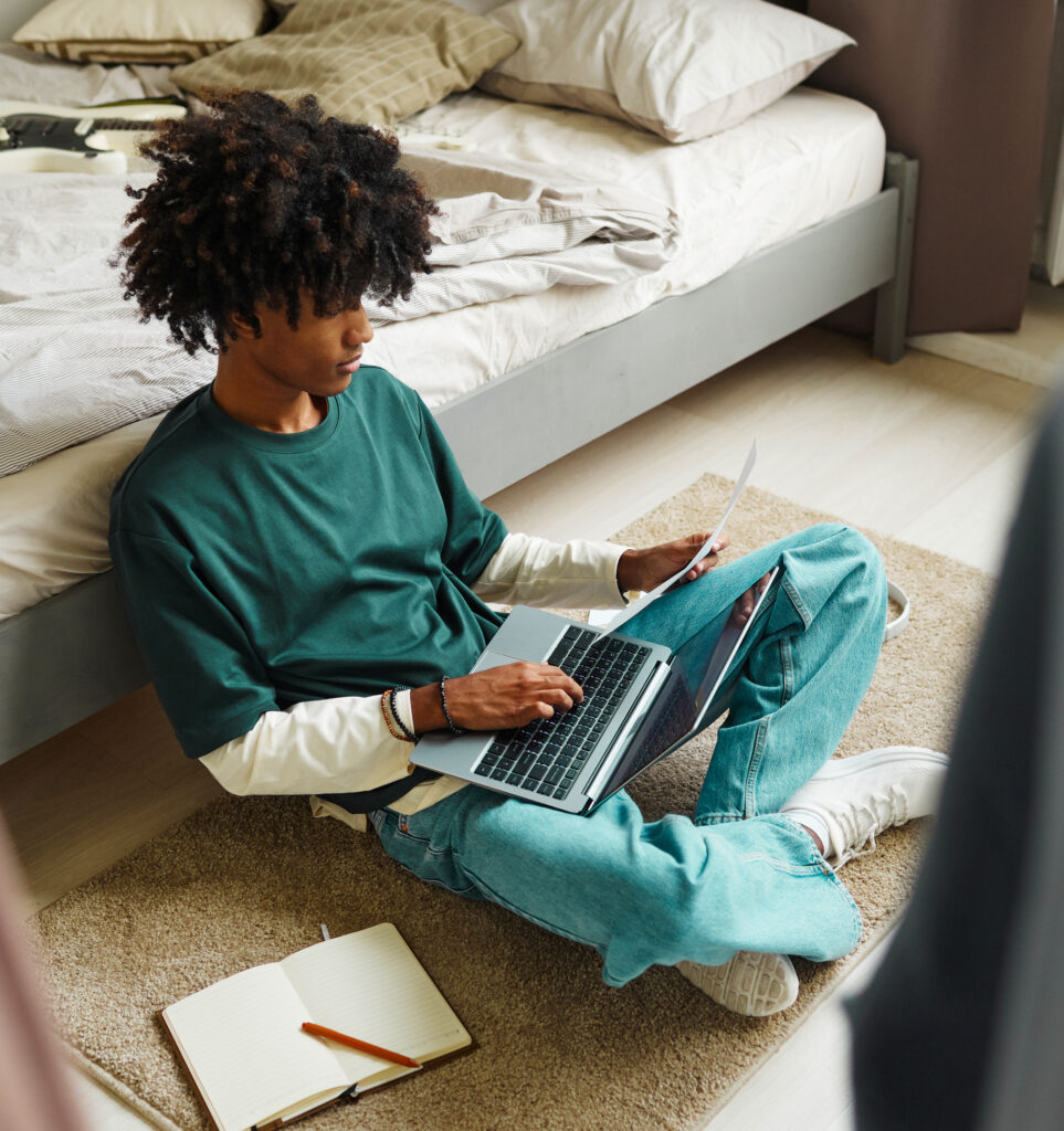 Teen sitting on floor with laptop in lap and paper in hand